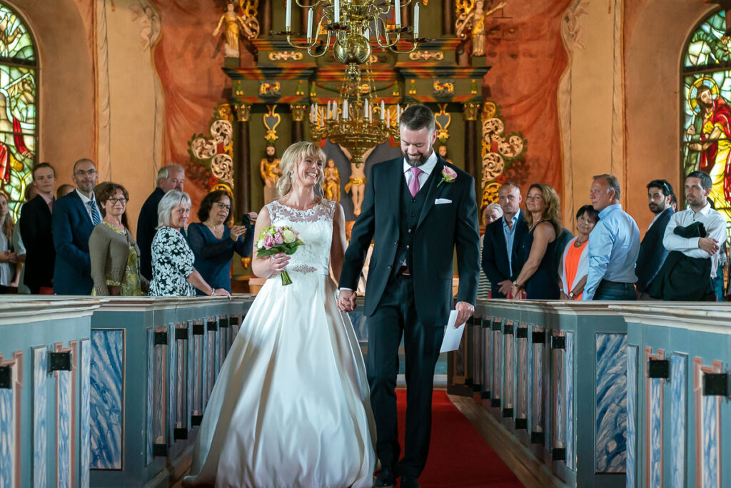 Bröllopspar går hand i hand ut ur kyrkan med gäster bakom sig