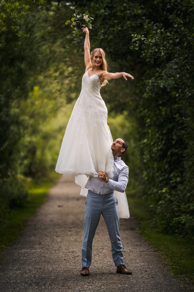 Bruden står upp på brudgummens axel i allén på Viksholmen i Arvika.