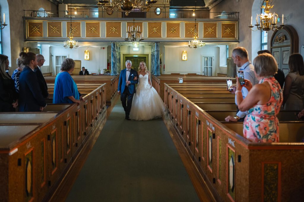 Bruden kommer arm I arm med sin far nedför altargången i Mikaelikyrkan i Arvika.