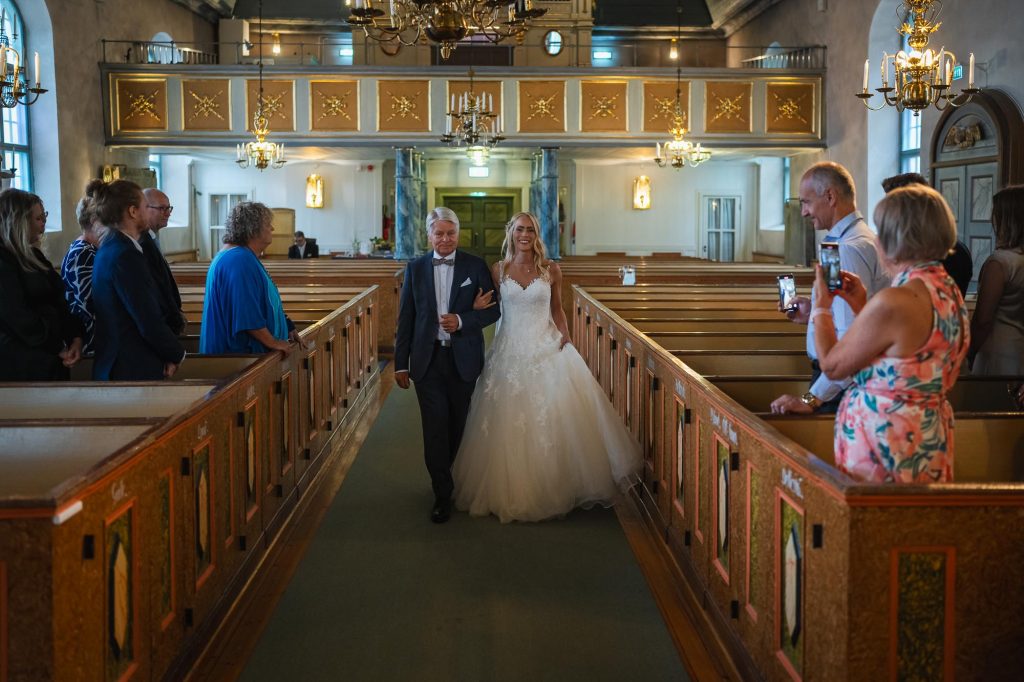 Bruden kommer arm I arm med sin far nedför altargången i Mikaelikyrkan i Arvika.