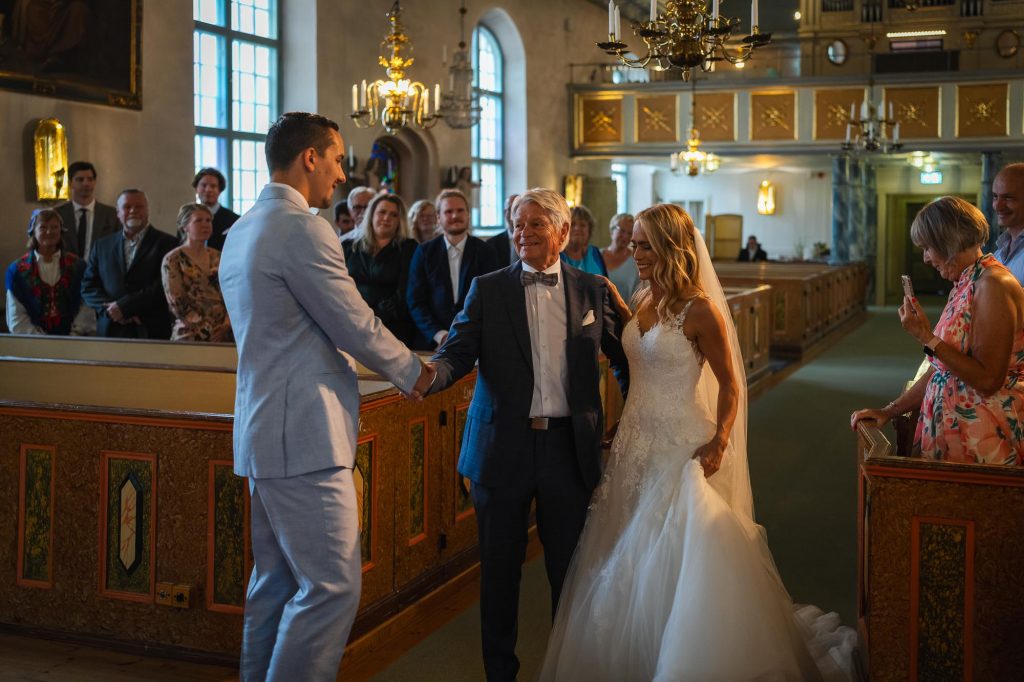 Brudens far lämnar över bruden till brudgummen i Mikaelikyrkan i Arvika.