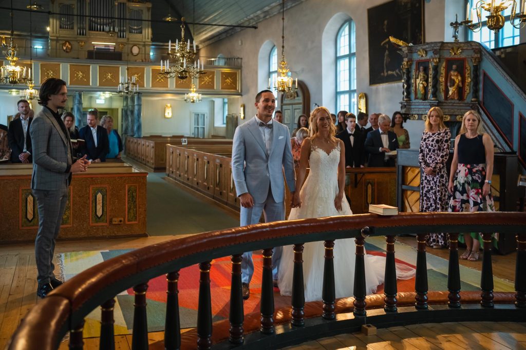Lyckligt nygift brudpar står framför altaret i Mikaelikyrkan i Arvika.