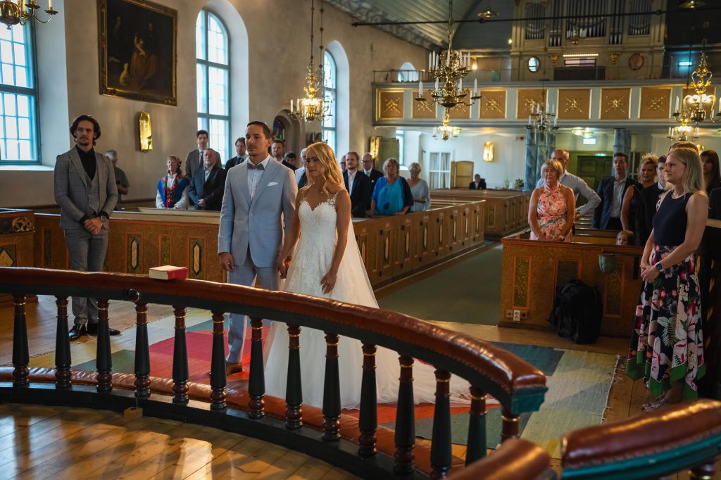 Lyckligt nygift brudpar står framför altaret i Mikaelikyrkan i Arvika.