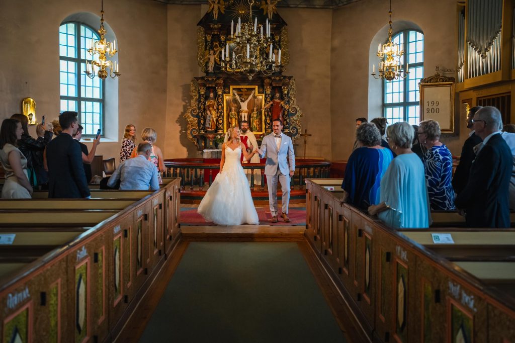 Brudparet går hand i hand nedför altargången i Mikaelikyrkan i Arvika.