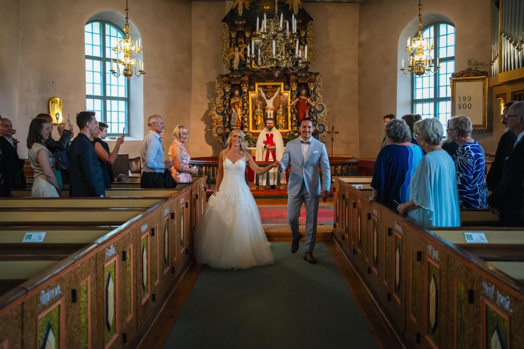 Brudparet går hand i hand nedför altargången i Mikaelikyrkan i Arvika.