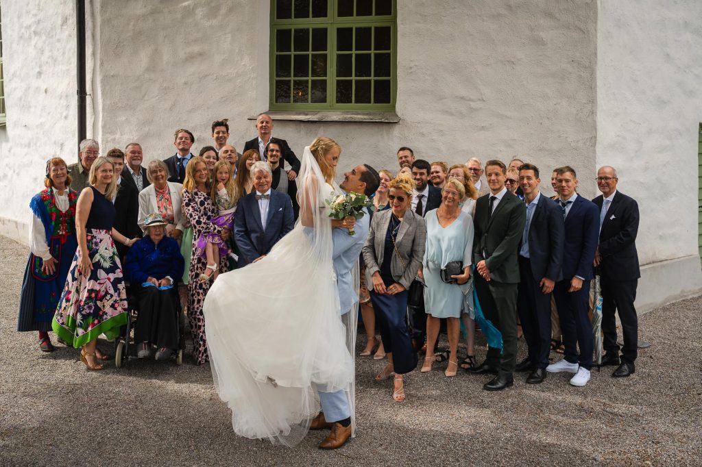 Gruppbild av brudparet och alla bröllopsgäster utanför Mikaelikyrkan i Arvika.
