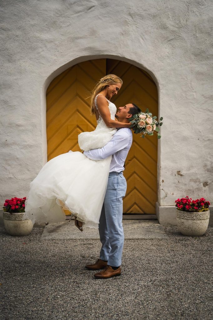 Brudgummen lyfter upp bruden utanför Mikaelikyrkan i Arvika.
