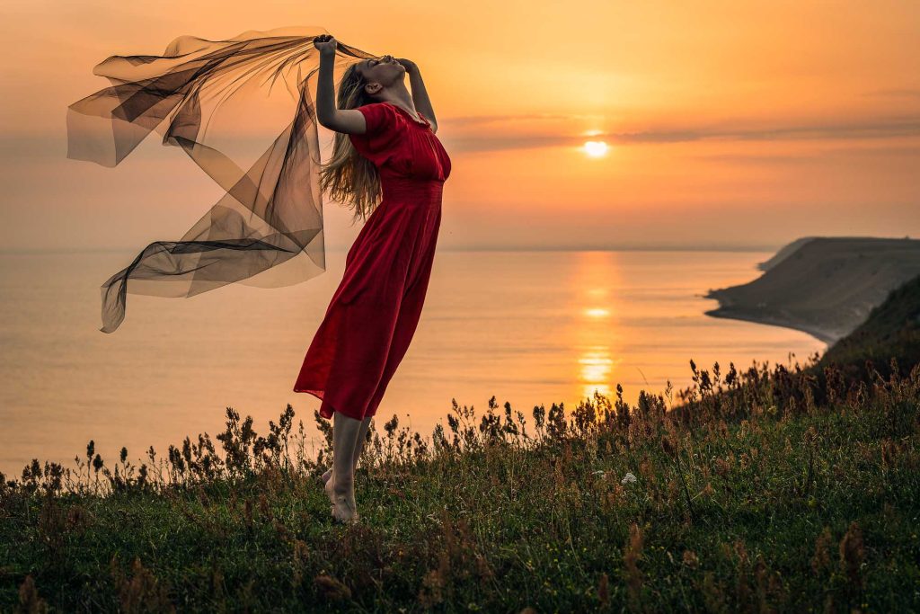 Ung kvinna i röd klänning med svart slöja vid solnedgång på Kåseberga