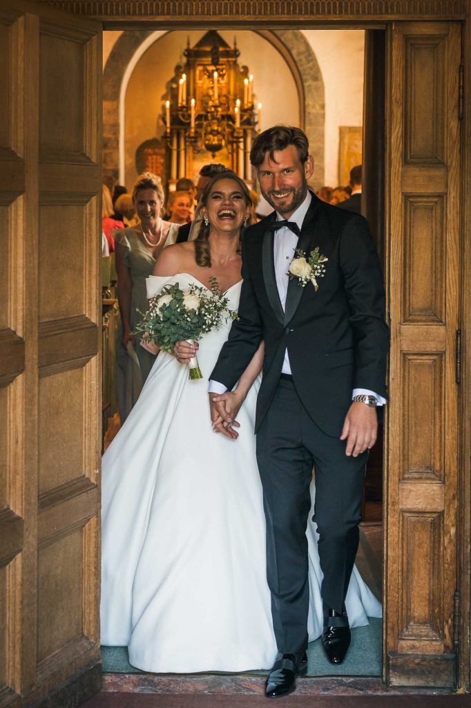 Bruden och brudgummen vandrar ut ur kyrkan med stora leende.