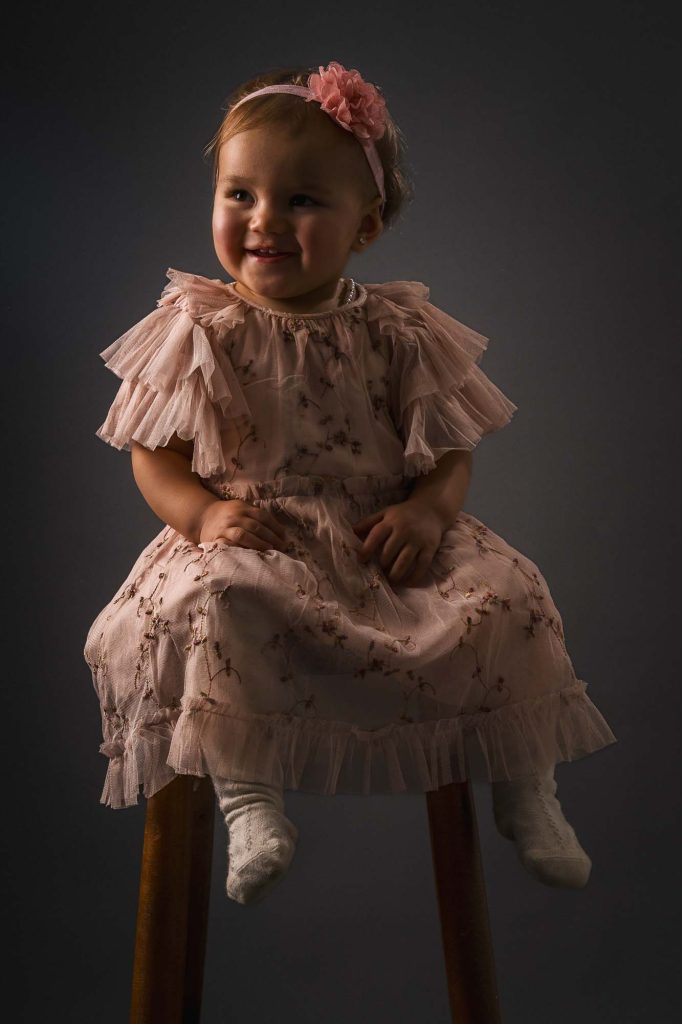 Liten flicka i rosa klänning på stol.