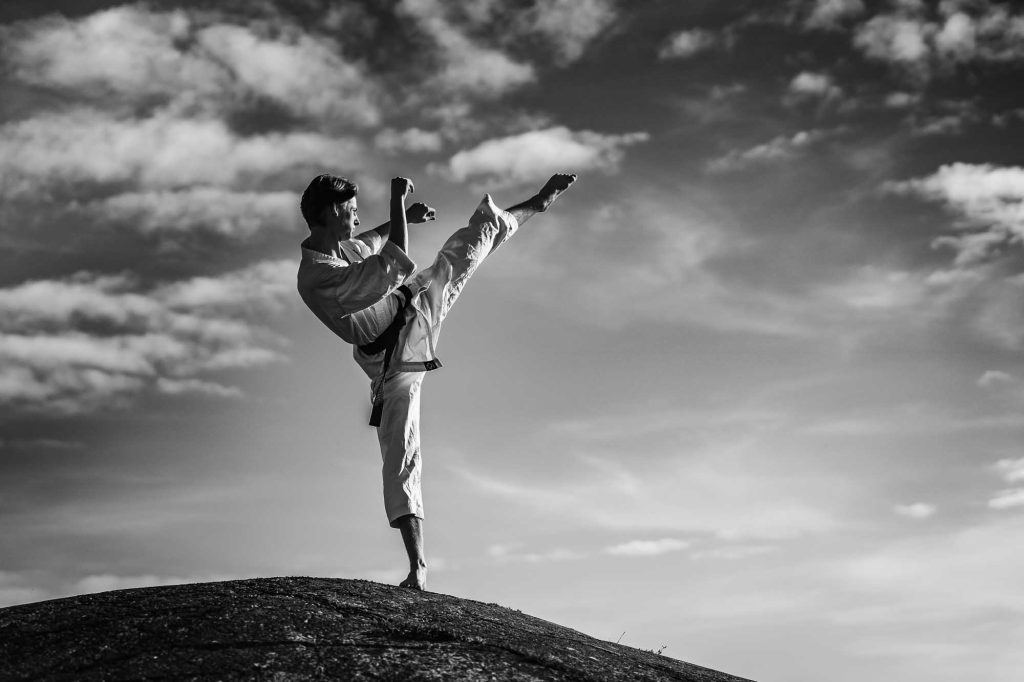 Svartvit bild av ung man gör karatekick stående på en klippa.