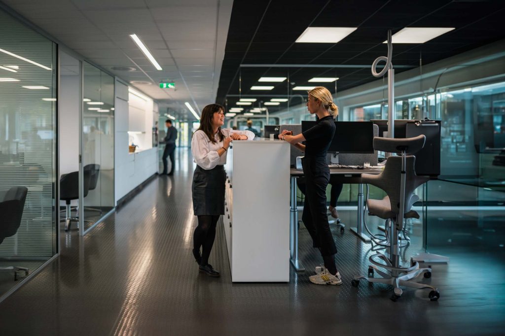 Foto av två kvinnor som står och diskuterar på jobbet.