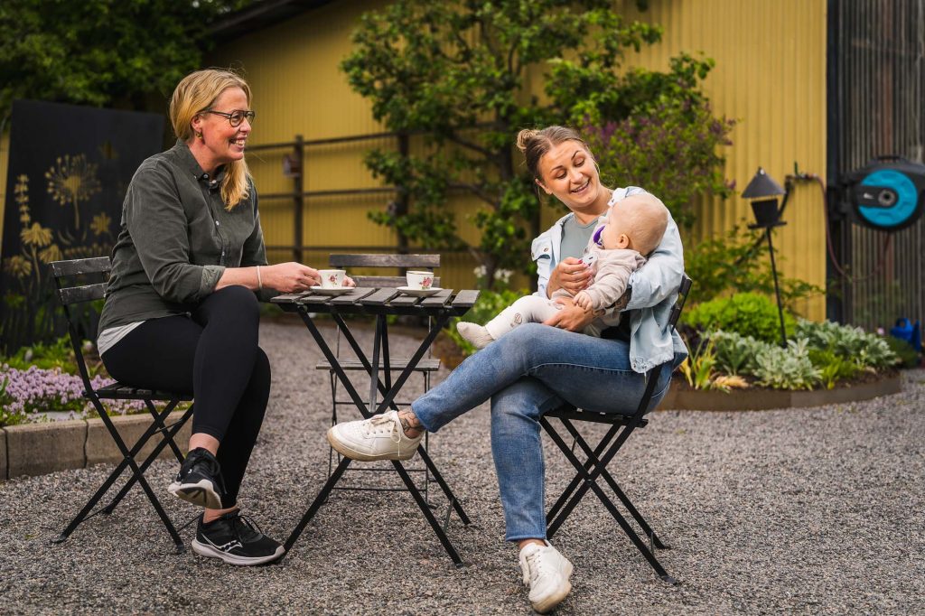Bild av kunder och barn som sitter och fikar utomhus på Högvalta handelsträdgård.