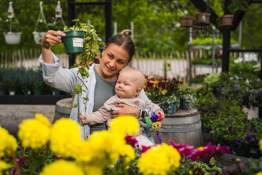 Mor med barn visar blomkruka för sitt barn på Högvalta handelsträdgård.
