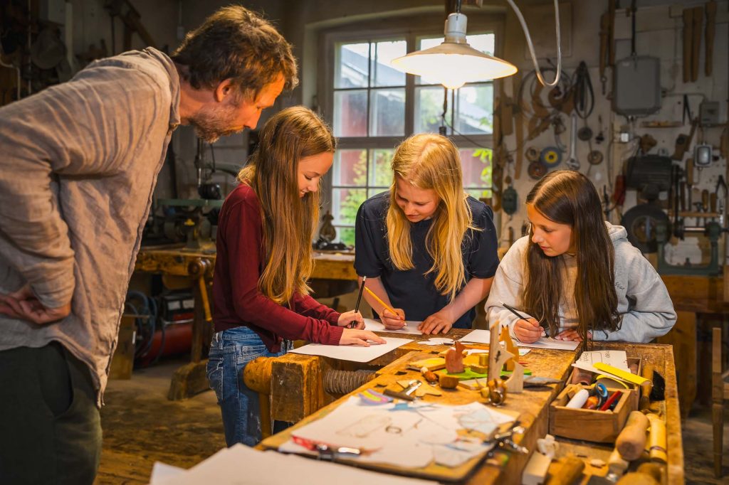 Handledare övervakar tre små tjejer som skapar namnbrickor på skaparverkstaden på Rackstadmuseet.