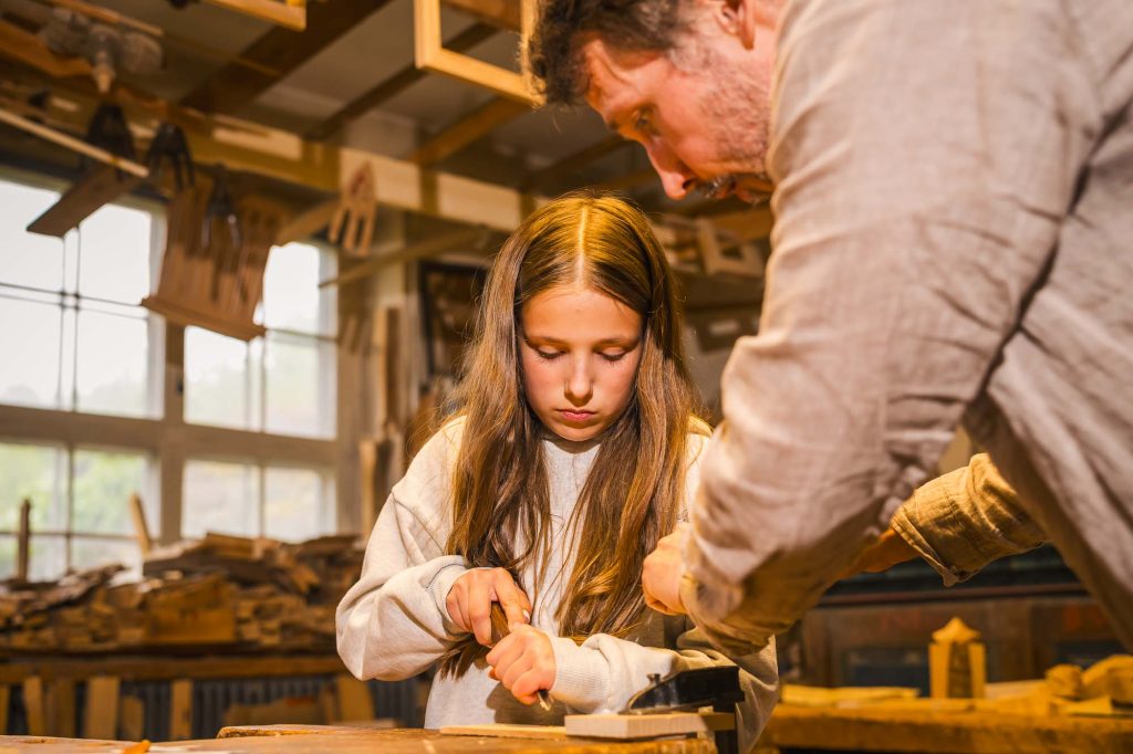 Handledare visar hyvel vid bänken i möbelsnickeriet på skaparverkstaden på Rackstadmuseet.
