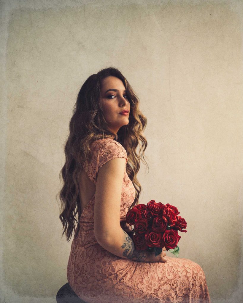 Kvinna i rosa klänning sitter på pall med röda rosor i knät.