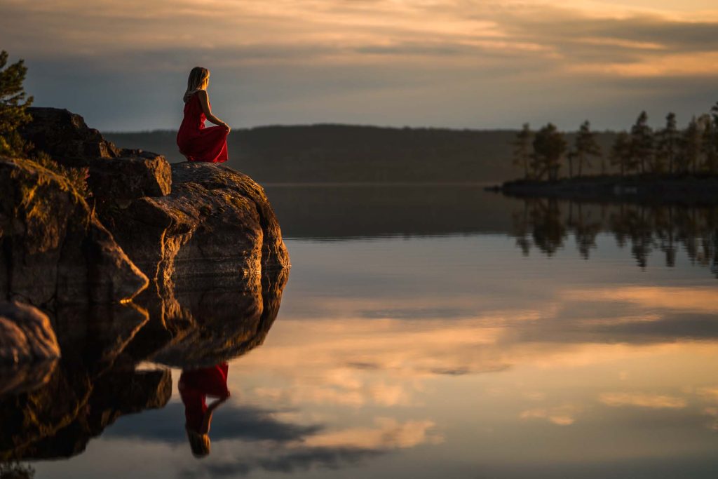 Ung kvinna sitter på sten och njuter av solnedgången vid Stora gla i Glaskogen Arvika