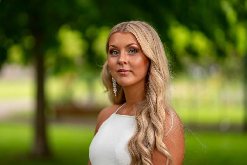 Studentporträtt av ung kvinna i vit klänning i Stadsparken i Arvika.