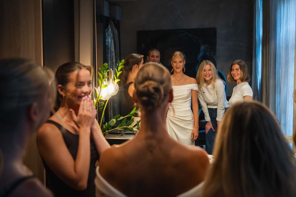 Brudens vänner beundrar bruden framför en spegel när hon fått på sig bröllopsklänningen.