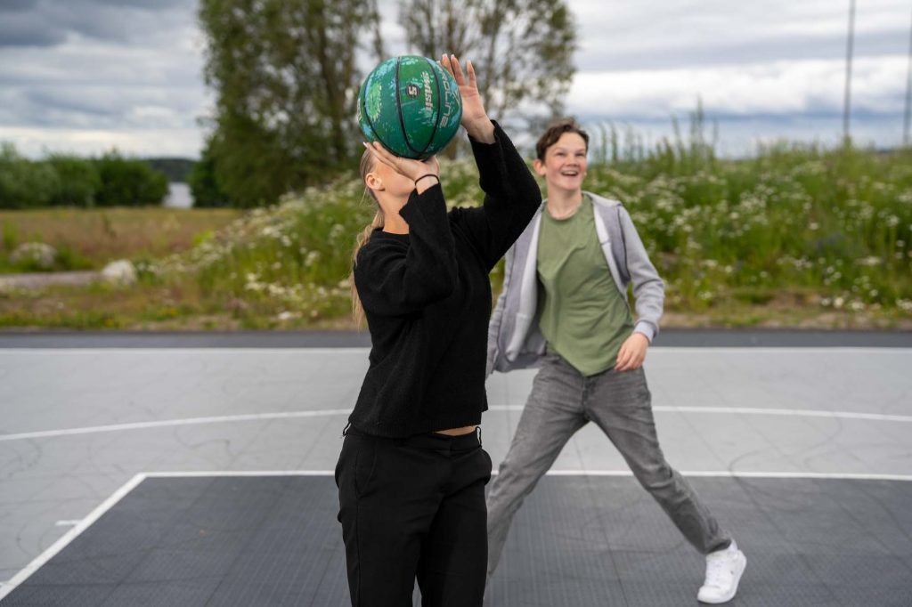 Tonåringar spelar basket på sportplanen i Arvikas hamnområde vid Kyrkviken.