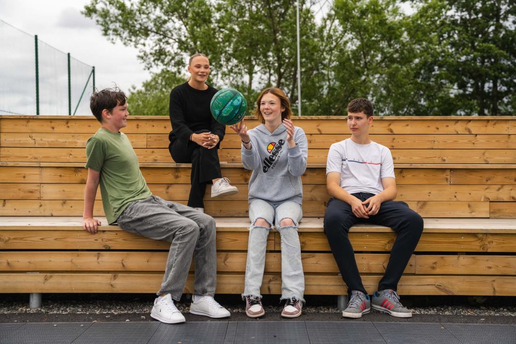 Fyra ungdomar vilar vid basketbollplanen i hamnområdet i Arvika.