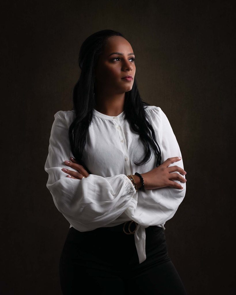 Mörkhyad kvinna i vit blus och svarta byxor med armarna i kors.