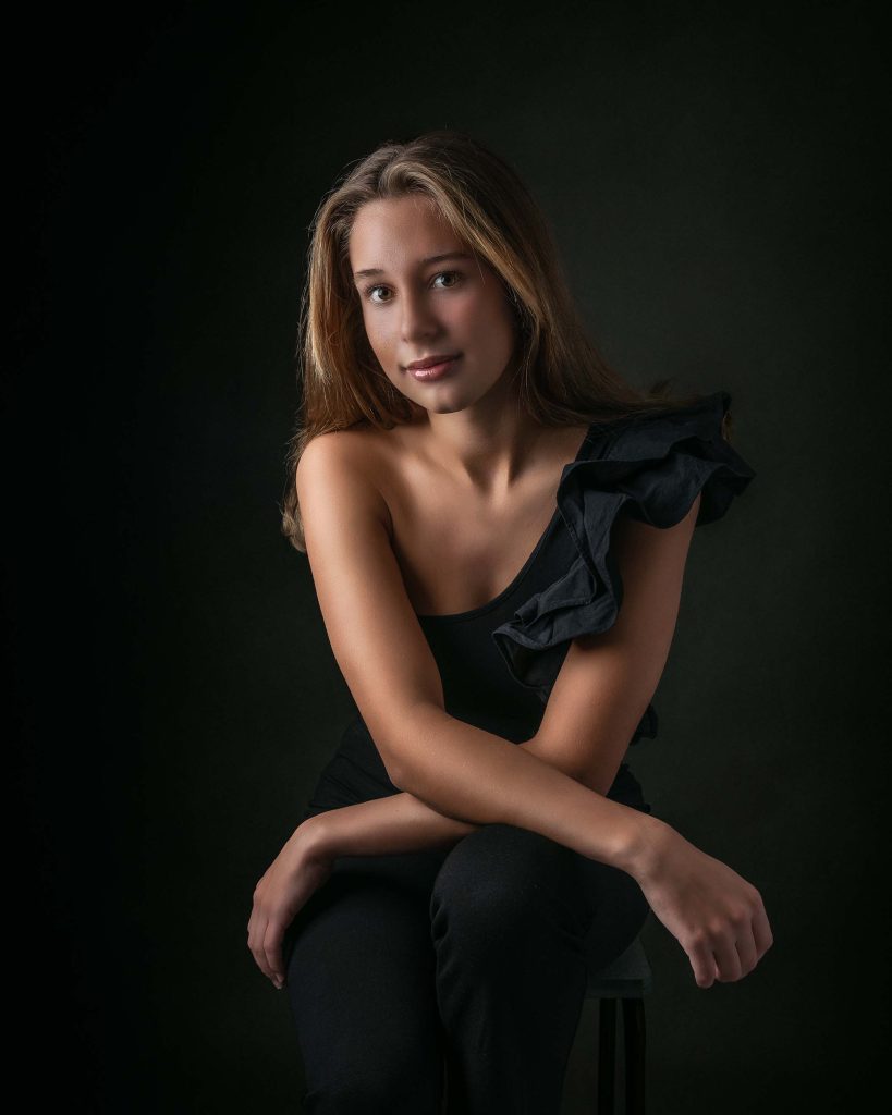 Ung kvinna i svart topp sitter på pall med armar i kors över knät.