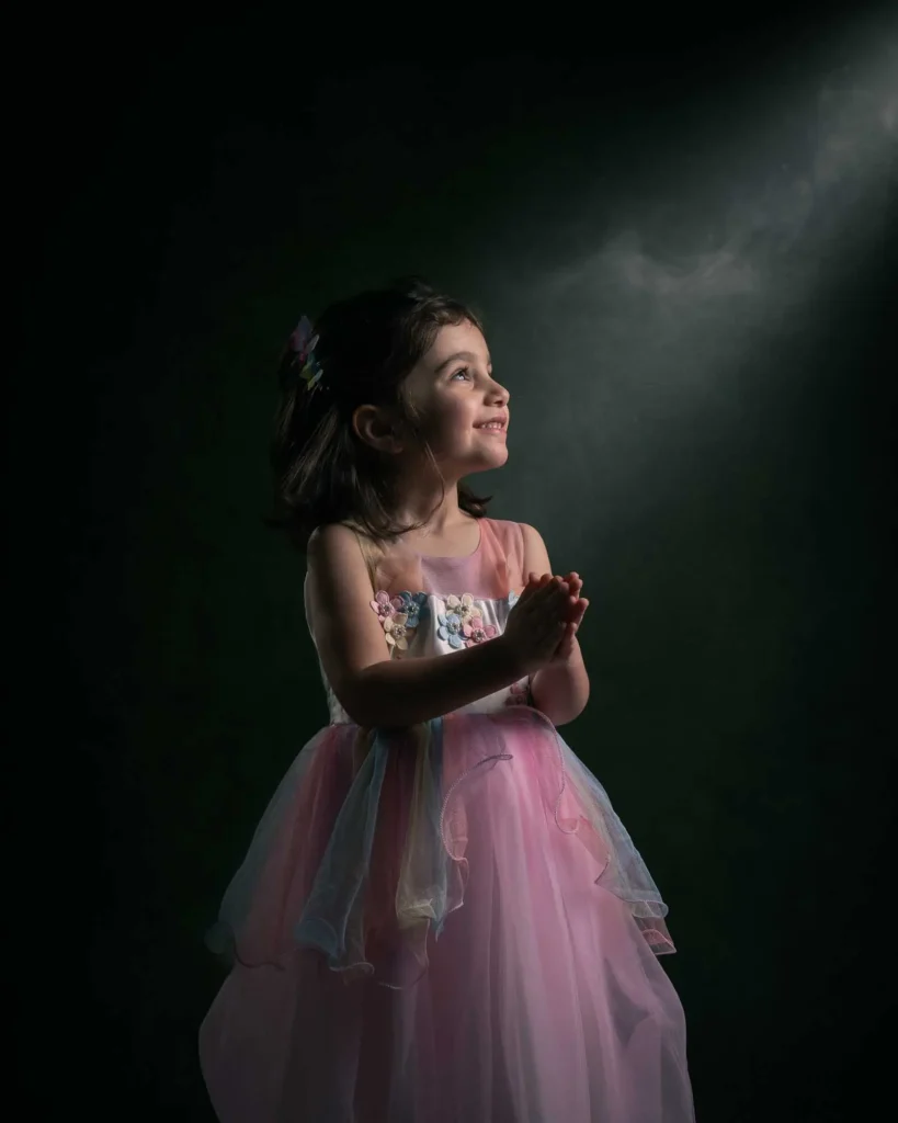 Ett drömskt porträtt av en flicka i en färgglad klänning som tittar upp mot ett magiskt ljus, fotat av en barnfotograf hos PixPep i Arvika.