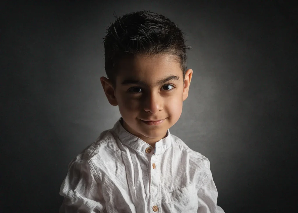 Ett väl ljussatt studioporträtt av en pojke i vit skjorta mot mörk bakgrund, fotograferad hos en barnfotograf i Arvika.