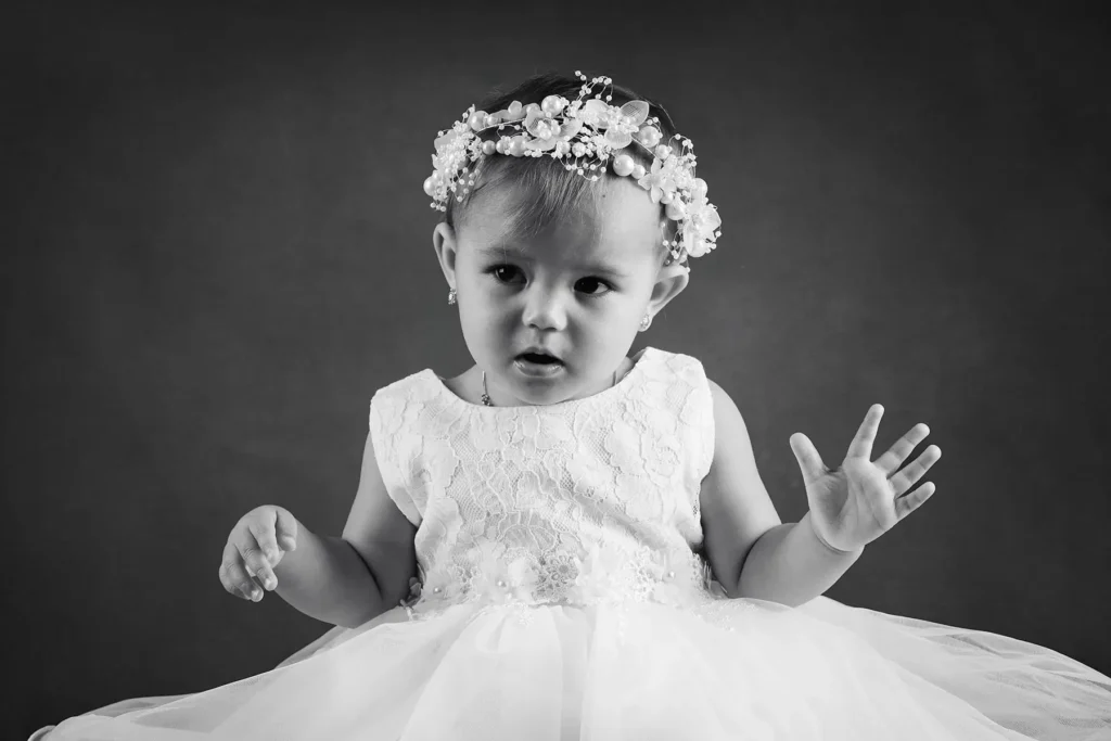 Svartvitt studiofoto på en liten flicka i vit spetsklänning med en vacker pärl- och blomkrans i håret, fotograferad i en studio i Arvika hos PixPep