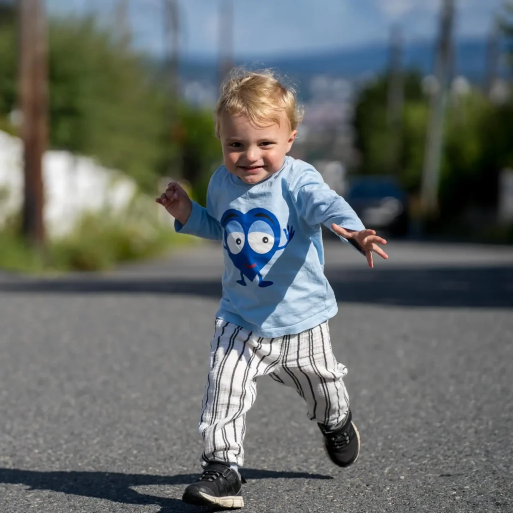 En glad liten pojke springer framåt på en asfalterad väg utomhus under en barnfotografering.