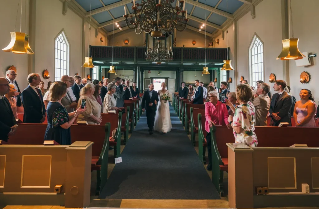 Bruden går uppför mittgången i Skillingmarks vackra träkyrka under ett bröllop i Värmland.