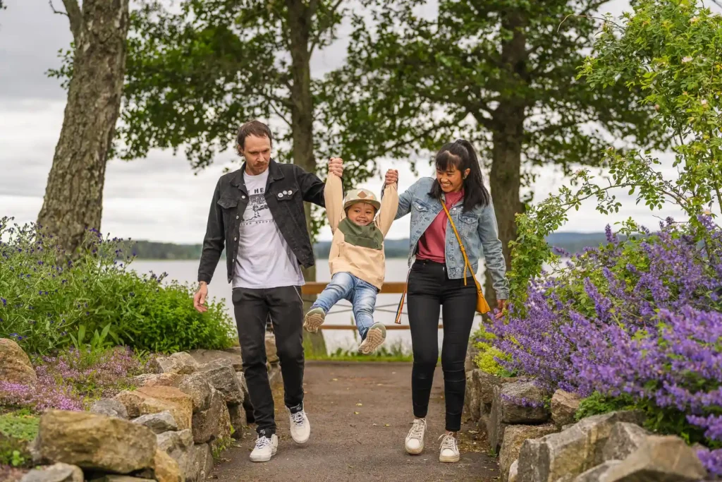 En familj leker och skrattar vid en blomsterkantad stig på Sågudden i Arvika. Professionell familjefotografering i Värmlandsmiljö fångad av PixPep.