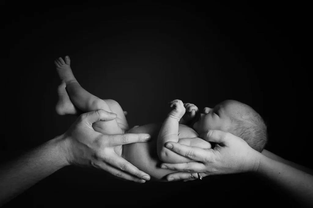Ett nyfött barn som vilar tryggt i sina föräldrars händer, förevigat i en stämningsfull svartvit studiobild i Arvika.