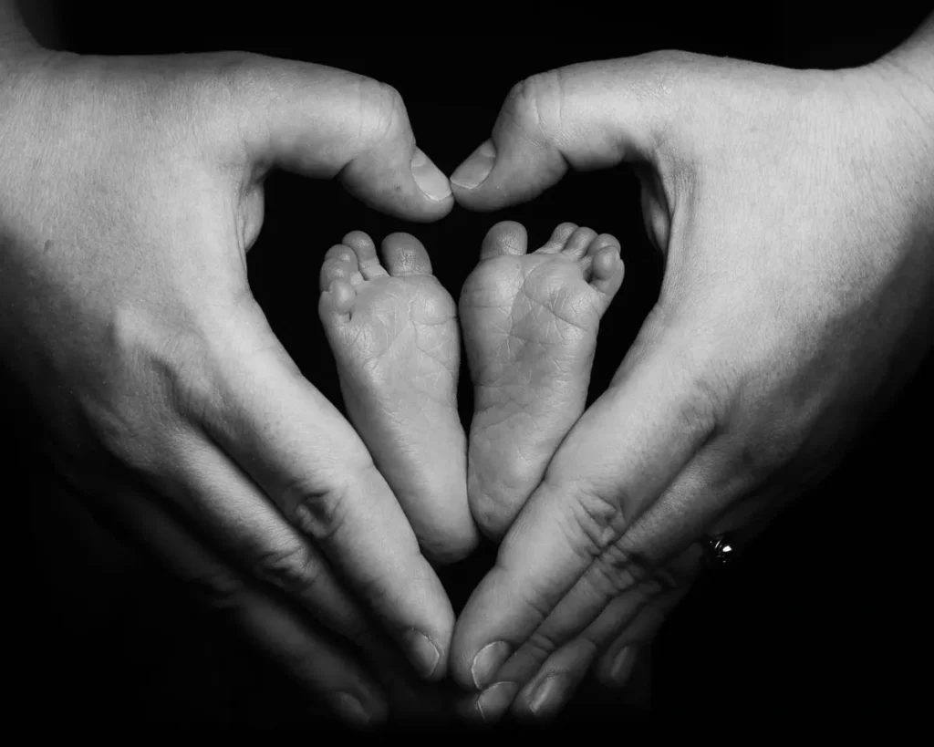 En känslosam detaljbild i svartvitt där föräldrars händer formar ett hjärta runt en babys fötter, fotad hos en professionell studiofotograf i Arvika.