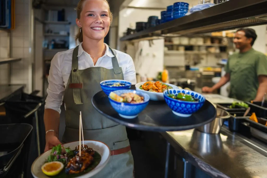 En leende servitris serverar mat i en restaurang, verksamhetsbild fotograferad av företagsfotograf i Värmland.