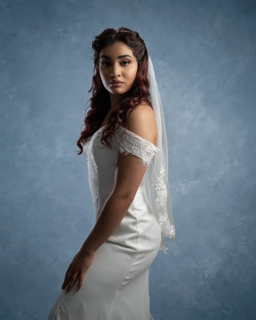 Professionellt bröllopsporträtt taget i studio med blå texturerad bakgrund, där bruden bär en off-shoulder klänning och slöja med spetsdetaljer.