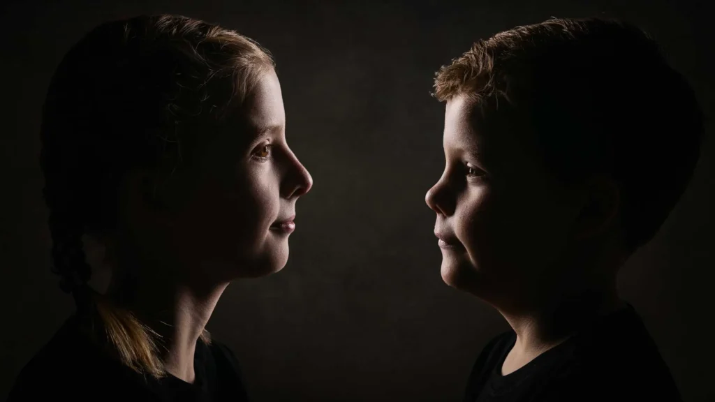 Ett konstnärligt porträtt av två barn i profil mot varandra med dramatisk ljussättning, fotat i Studio PixPep i Arvika.