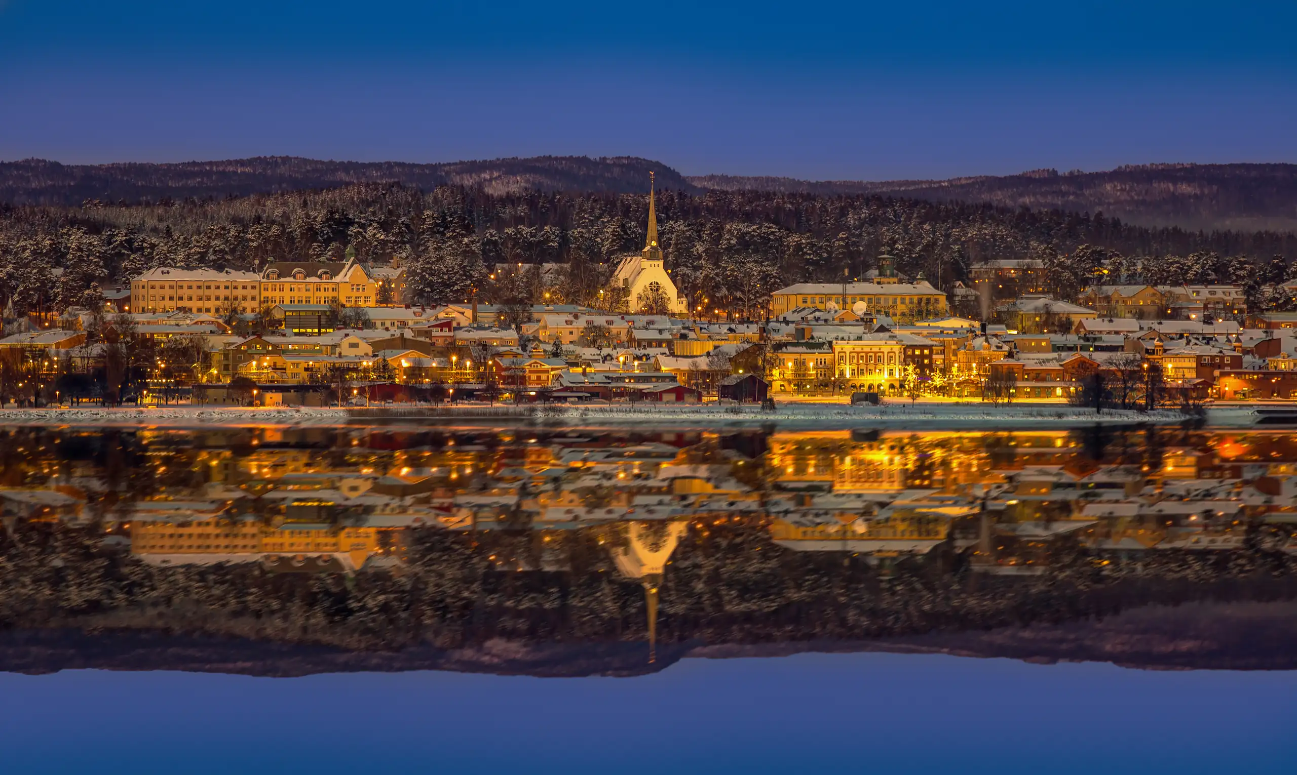 Speglat vinterlandskap av Arvika stad vid skymning över Kyrkviken.