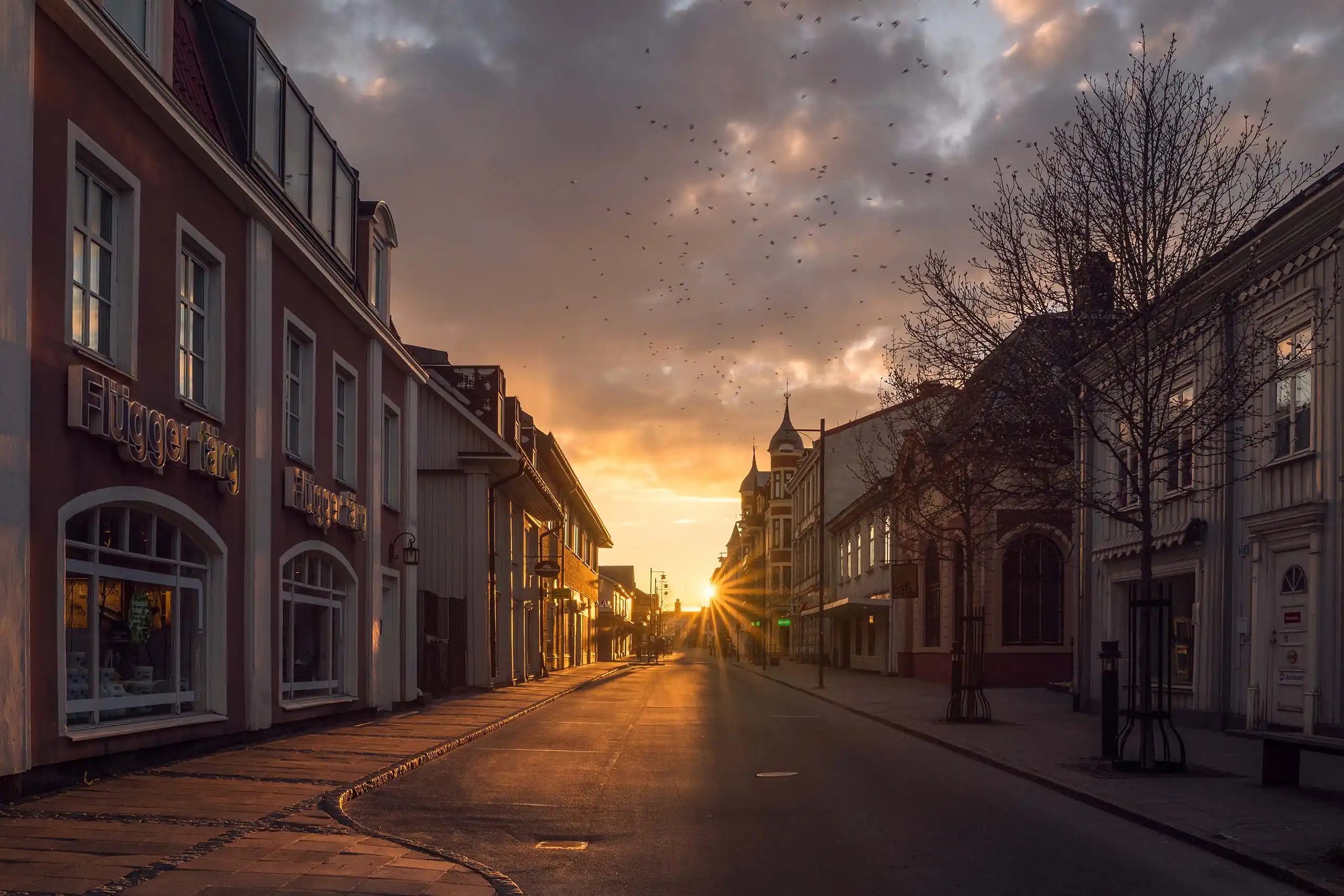 Solnedgång över Storgatan i Arvika där solstrålarna bryter fram mellan de vackra byggnaderna, fotograferat av en professionell fotograf för Arvika stadsbilder.