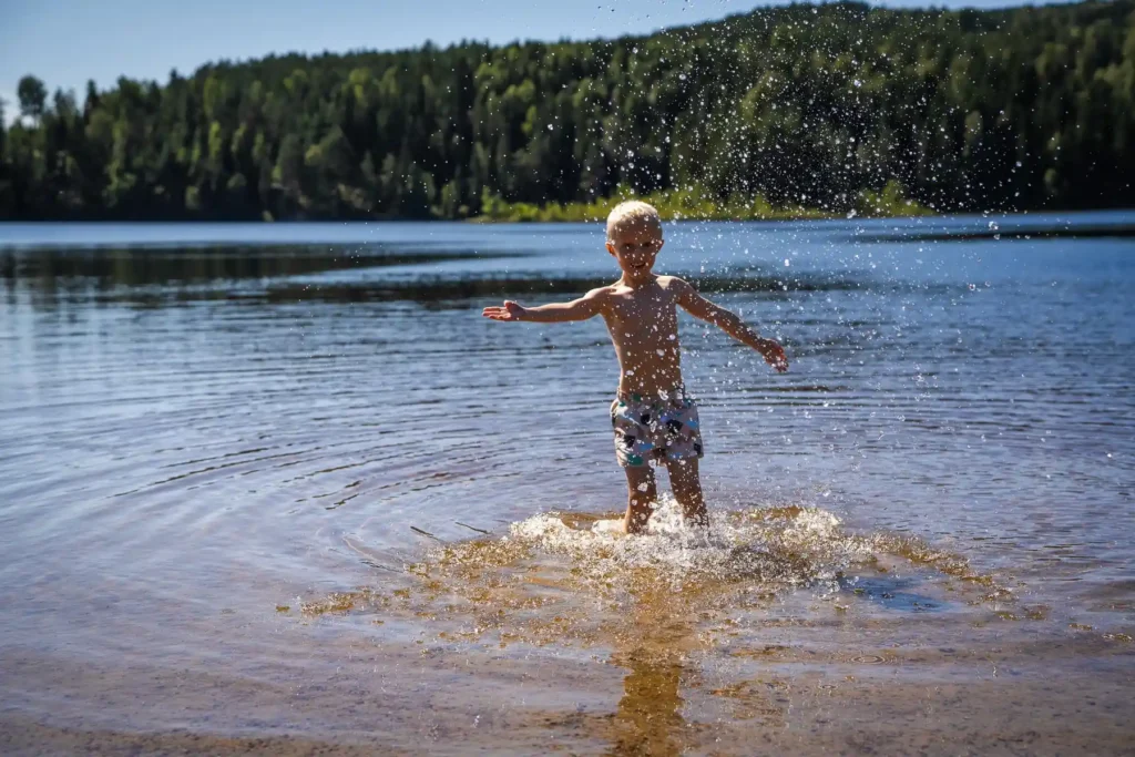 En liten pojke leker i vattenbrynet vid Kolsjöns badplats under en solig sommardag i Värmland.