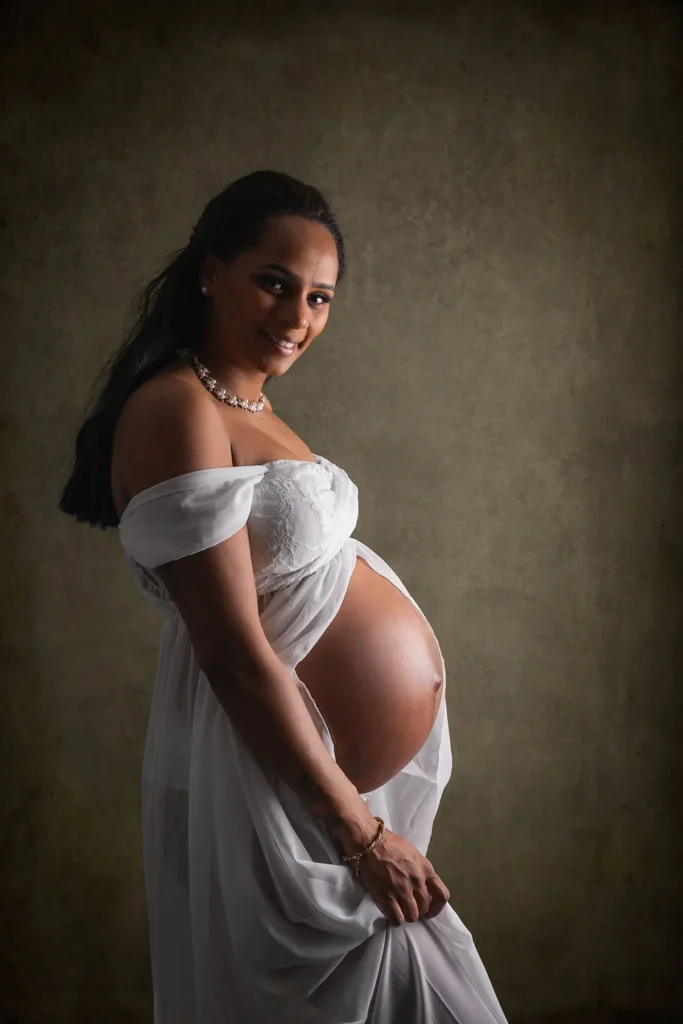 Ett elegant studioporträtt av en leende gravid kvinna i vit klänning mot en mörk bakgrund, fotograferad av PixPep Gravidfotograf i Arvika.