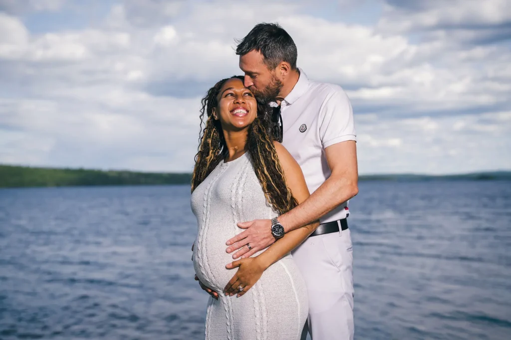 Ett kärleksfullt par poserar vid sjön i Tasebo under en gravidfotografering i Värmland, där mannen pussar kvinnan på pannan.